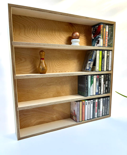 A wooden cassette tape shelf with four rows, displaying various cassette tapes and a decorative item on the top shelf.